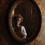 A woman in period attire reflects in a vintage mirror, creating an aristocratic ambiance.